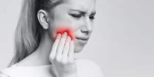Woman touching cheek with red spot showing pain area