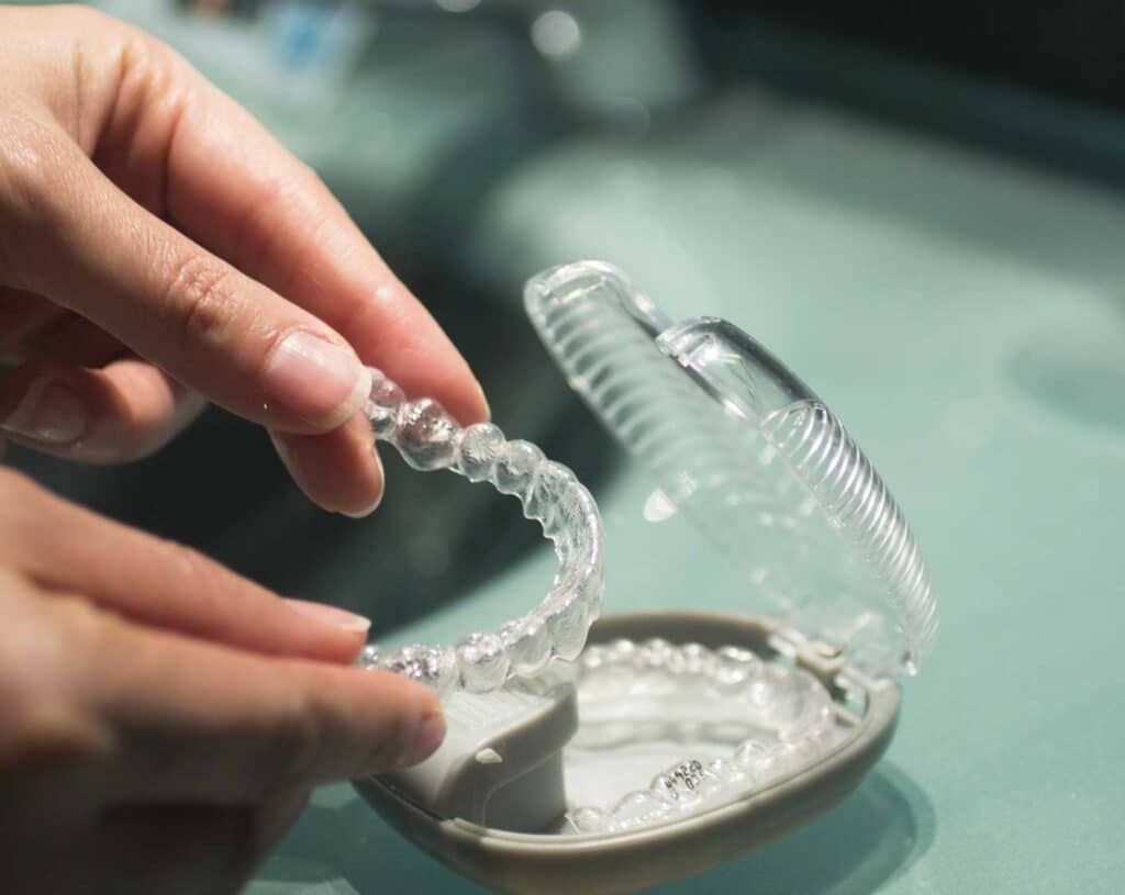 hands putting retainer in case at bathroom sink to illustrate orthodontic retention programs